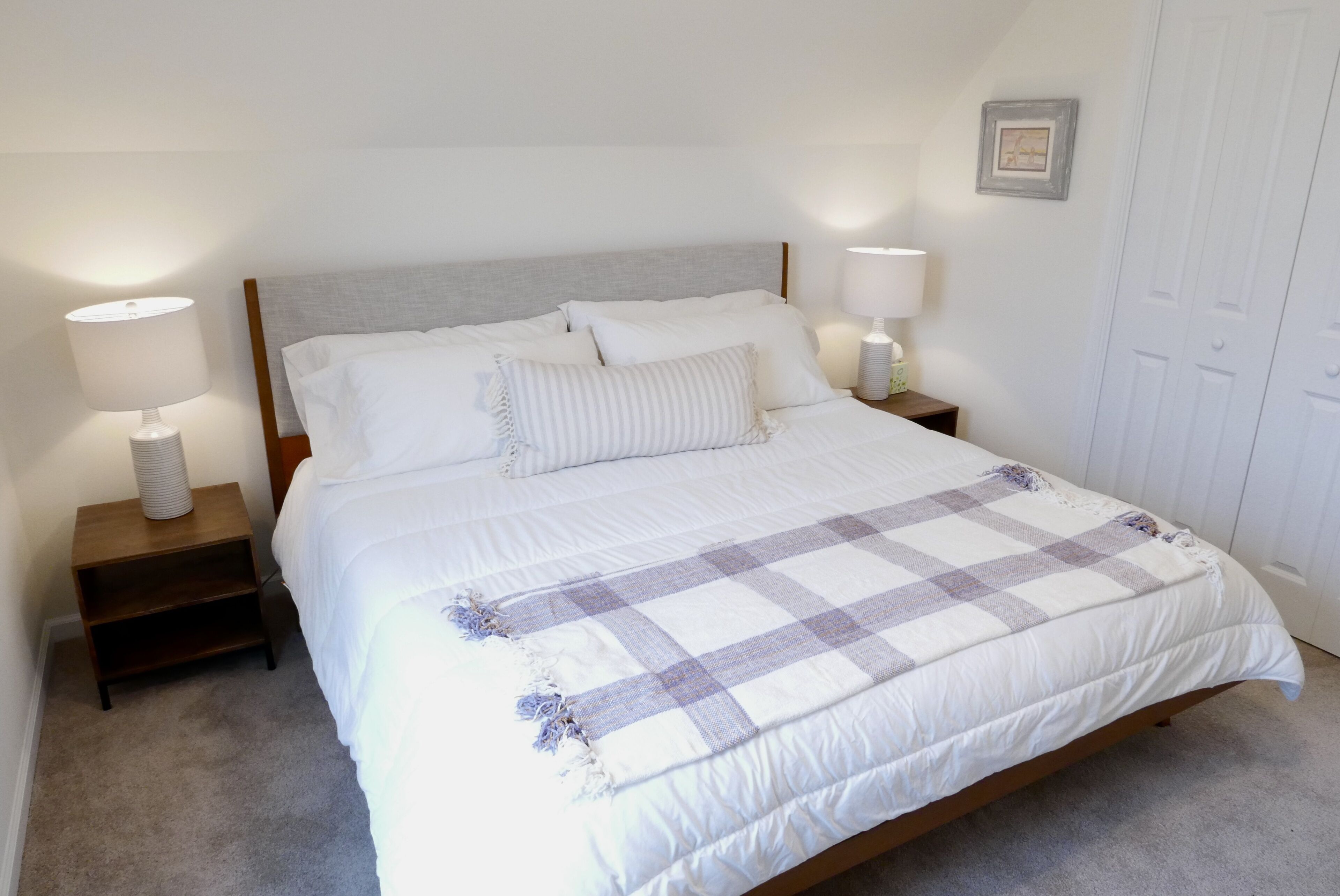 A neatly made bed with a checkered blanket, two bedside lamps, and a small wooden nightstand.