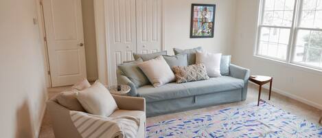 A living room with a sofa, a chair, a patterned rug, a small table, and a ceiling fan.