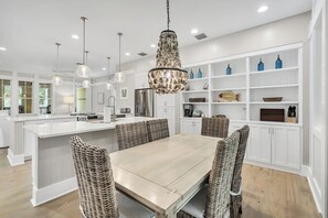 A modern kitchen with a central island, white cabinetry, and a dining area with wicker chairs.