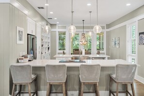 A modern kitchen with a central island, bar stools, pendant lighting, and a view of the outdoors.