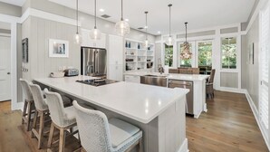 Cozinha moderna com uma ilha grande, banquetas, iluminação pendente e vista para o exterior.