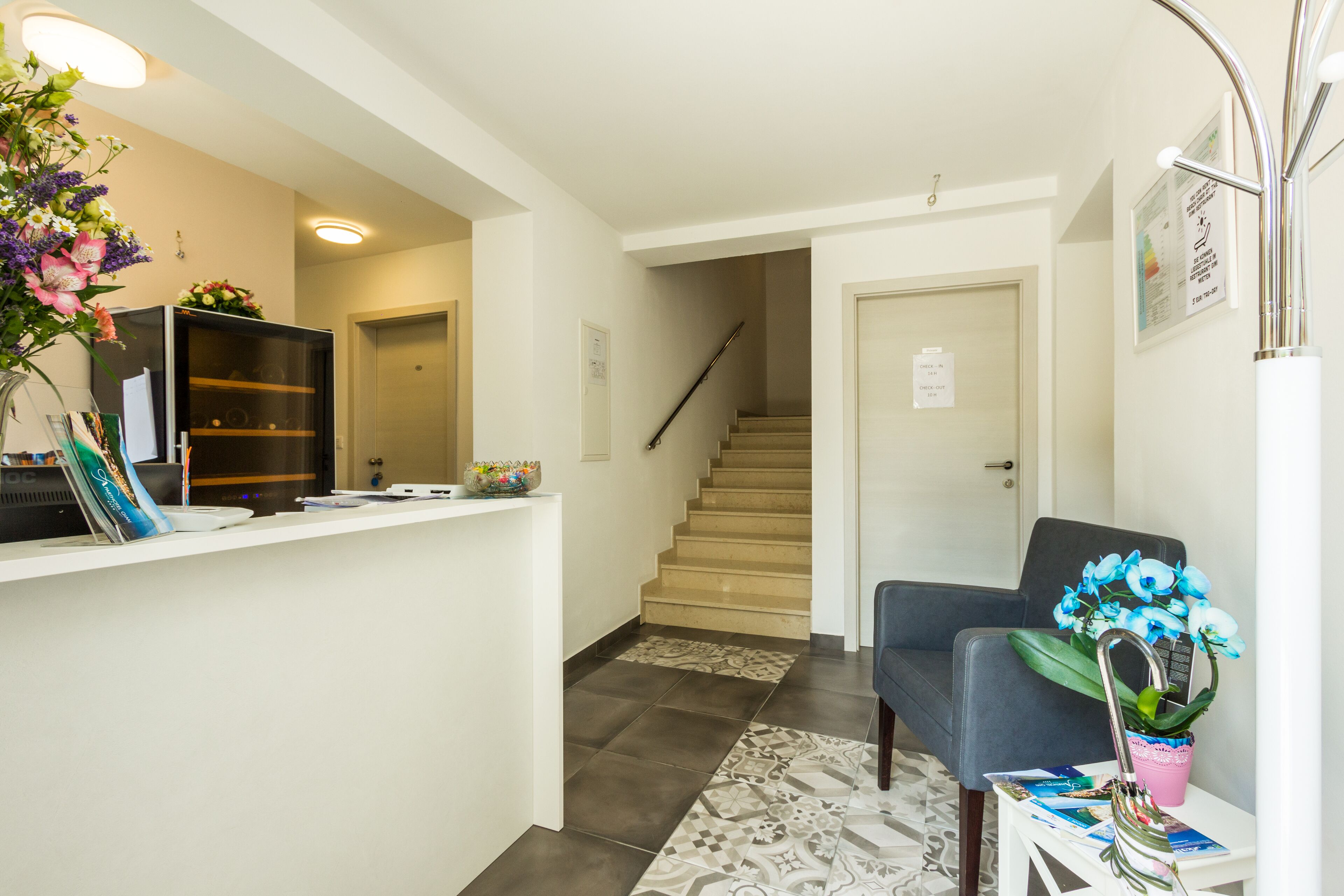 A reception area with a counter, a staircase, a blue chair, and a potted plant.