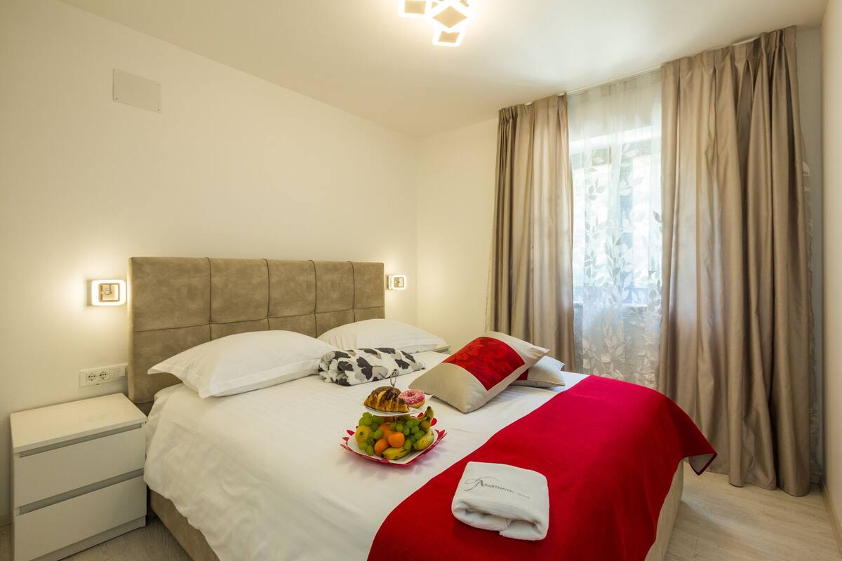 A hotel room with a bed, a bedside table, a fruit basket, and a red blanket.