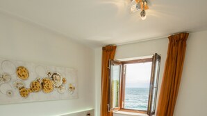 A neatly made bed with white and orange bedding, a red rug, and a decorative wall piece. - Aparthotel Gimi (Moscenicka Draga)