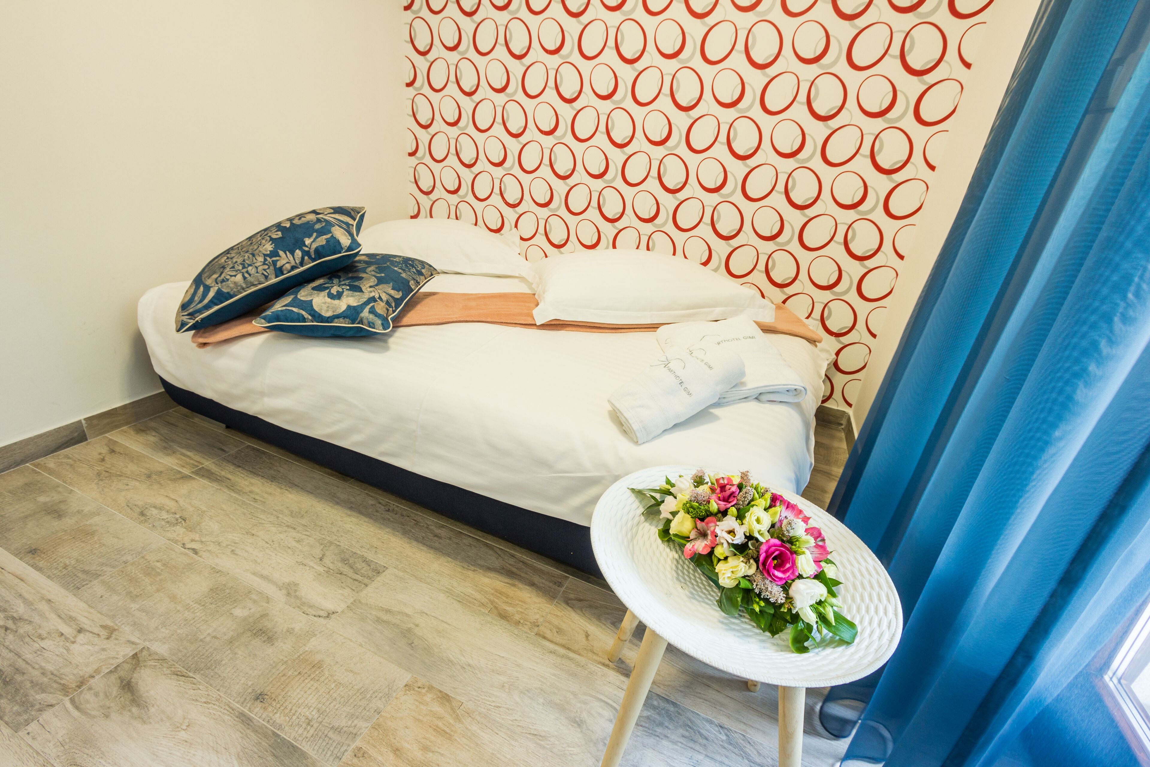 A neatly made bed with pillows and a floral arrangement on a small table beside it.
