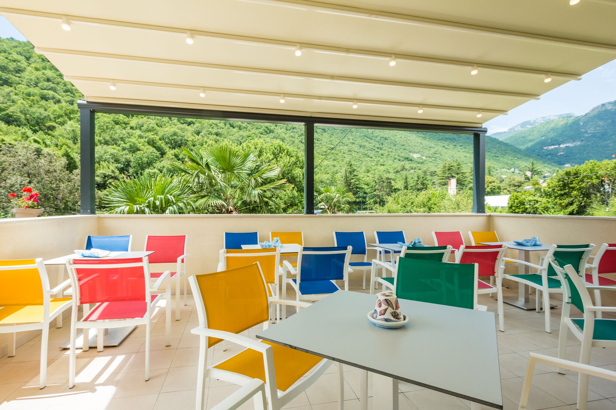 An outdoor patio with colorful chairs and tables, overlooking a lush green valley.