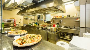 A commercial kitchen with stainless steel appliances, two pizzas on the counter, and various cooking utensils and ingredients. - Aparthotel Gimi (Moscenicka Draga)