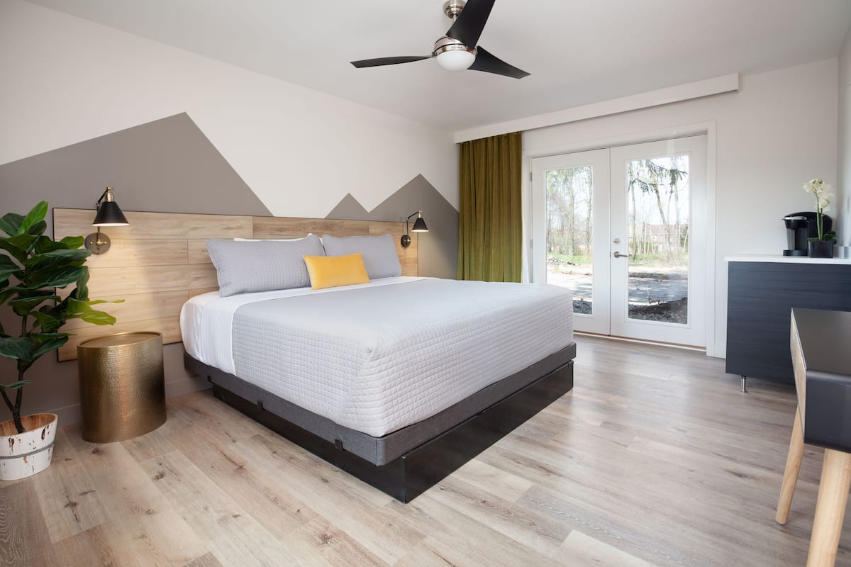 Une chambre à coucher moderne avec un lit, des lampes de chevet, un ventilateur de plafond, une vue à travers une porte-fenêtre coulissante et une plante.