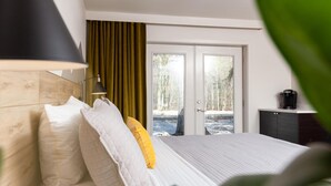 A hotel room with a bed, a desk with a coffee maker, and a view of a natural landscape through the door. - 4411 Inn & Suites (Michigan City)