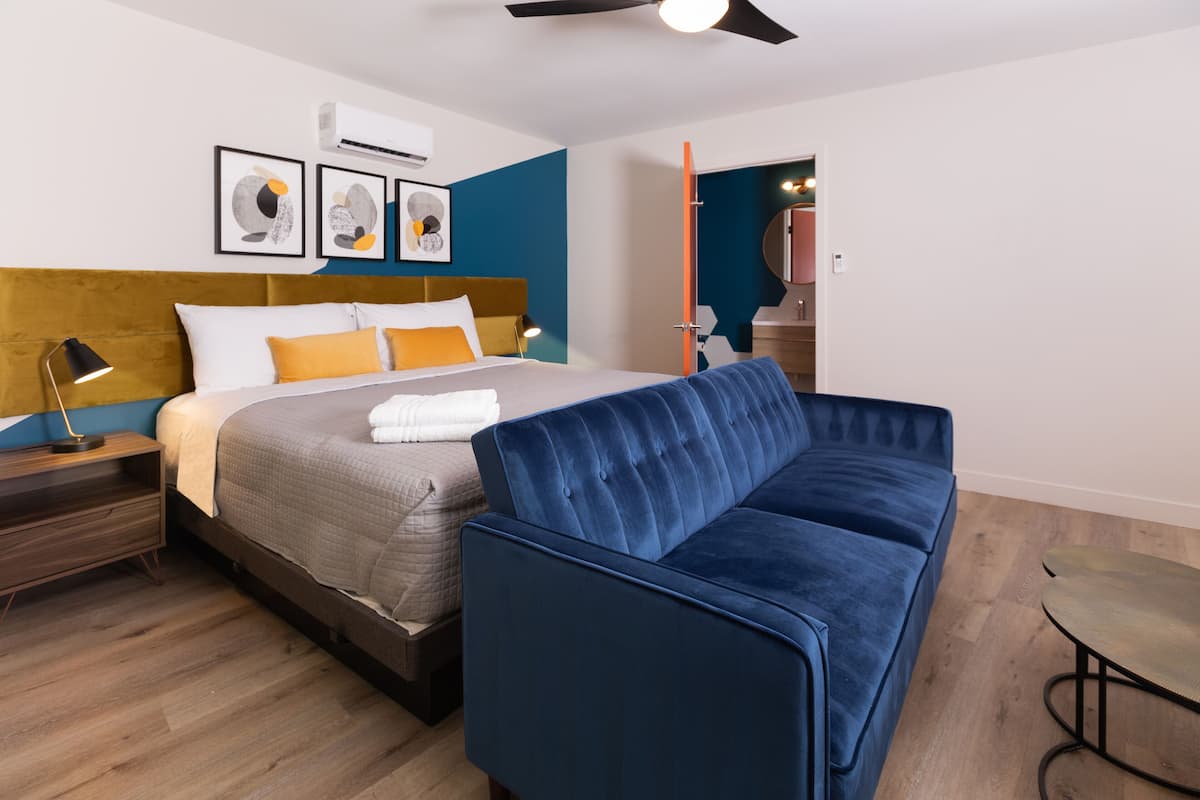 Une chambre à coucher moderne avec un lit, un canapé bleu, une table de chevet en bois et une petite table.