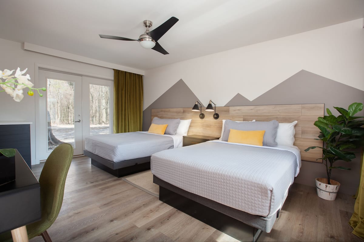 Une chambre d’hôtel avec deux lits, un bureau, une chaise, un ventilateur de plafond et une plante en pot.