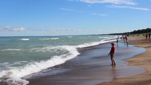 A beach with people walking along the shore and waves crashing onto the sand. - 4411 Inn & Suites (Michigan City)