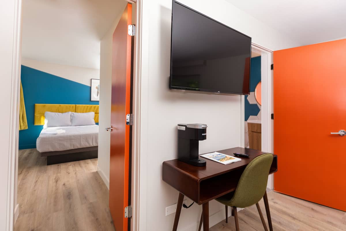 Une chambre d’hôtel avec un lit, un bureau doté d’une machine à café, une télévision et une porte orange.