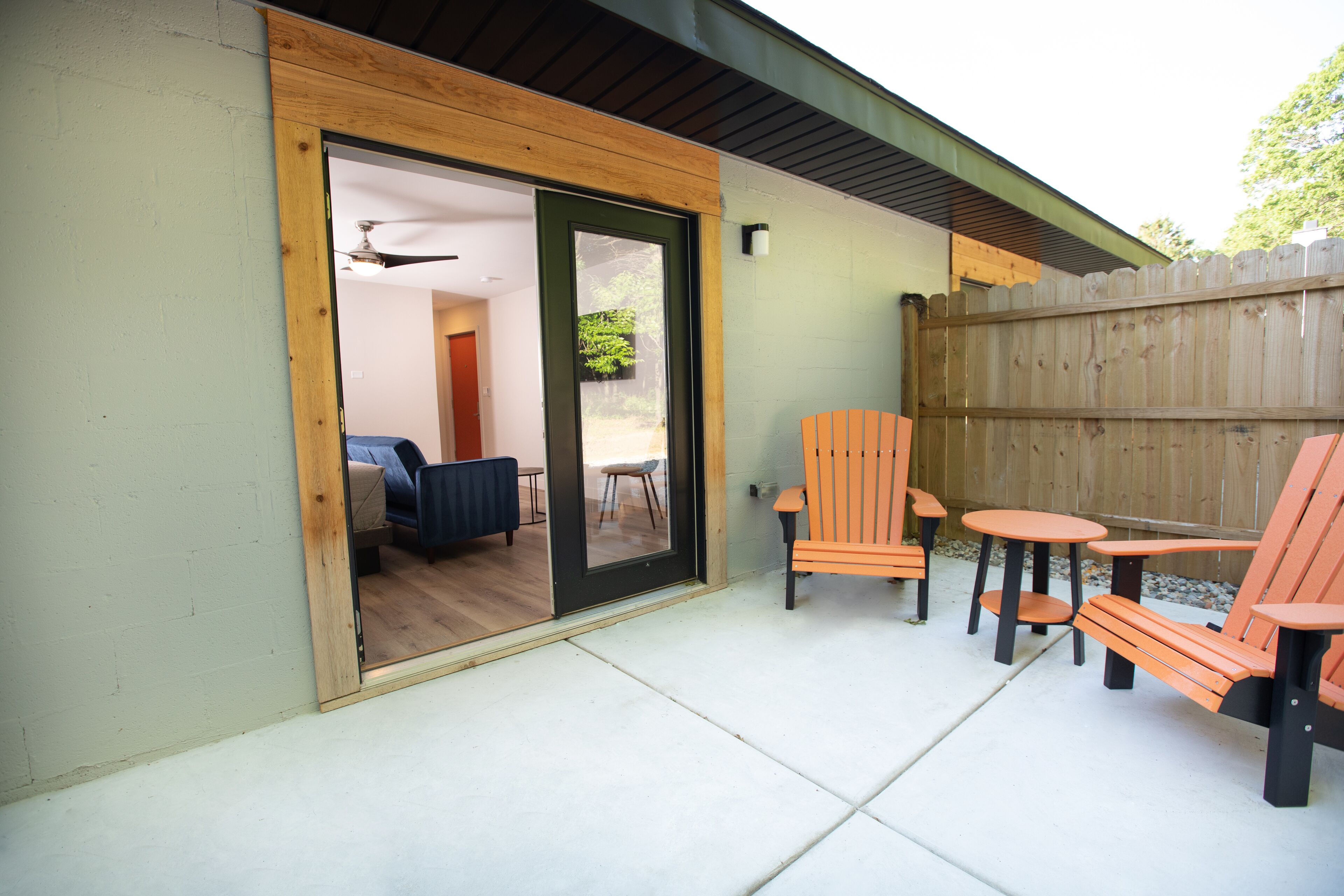 An outdoor patio with a wooden deck, a sliding glass door leading to an interior room, and a wooden fence.