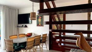 Un comedor con una mesa redonda, sillas de mimbre y un televisor fijado a la pared.
