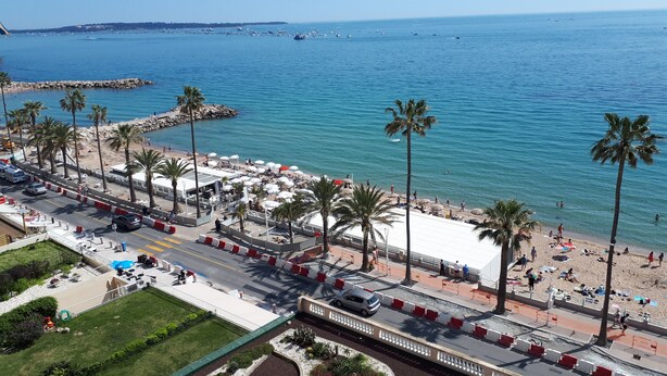 A coastal promenade with palm trees, beach umbrellas, and a view of the sea.
