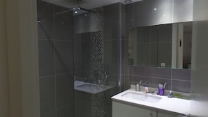 A modern bathroom with a glass shower enclosure, a white sink, and a large mirror.