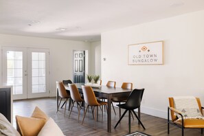 A modern dining area with a wooden table and chairs, a white wall with a framed sign, and a door leading to another room. - Awesome House with Large backyard + Pool + Free Pool heating all year long (Scottsdale)