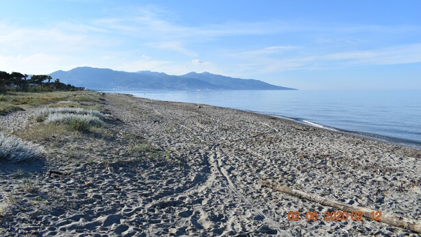A beach with a clear view of mountains in the distance, a sandy shore, and a timestamp indicating the date and time. - Beach<100m. Air conditioning. Wifi. Enclosed garden. bbc. Parking.opt car. No. of activities (borgo)