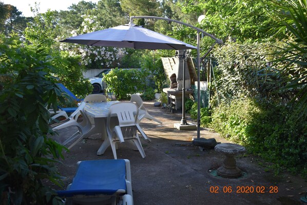 An outdoor patio area with a round table and chairs, a large umbrella, and a birdbath.