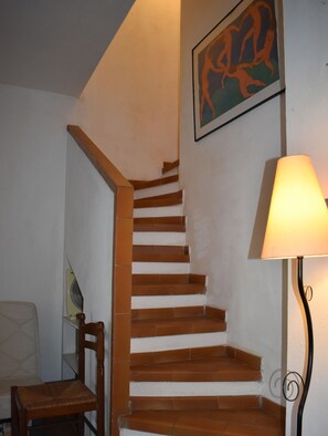 Eine Treppe mit Holzbodenstufen und weißen Wänden, ein Stuhl, eine Lampe und ein gerahmtes Kunstwerk.