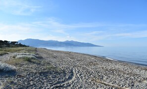 Una spiaggia con una vista chiara delle montagne sullo sfondo, una riva sabbiosa e un timestamp che indica data e ora.