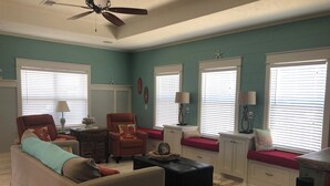 A living room with a sofa, armchair, and ottoman, a ceiling fan, and a window with blinds. - Relax and unwind in this Beautiful and Spacious smoke-free and pet-free home! (Port Bolivar)