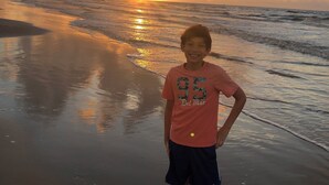 A person standing on a beach with the sun setting in the background. - Relax and unwind in this Beautiful and Spacious smoke-free and pet-free home! (Port Bolivar)