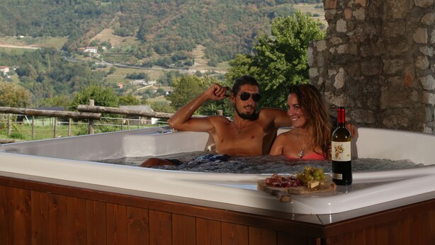 A hot tub with a wooden deck, a bottle of wine, and a plate of food.