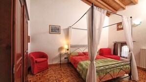 A four-poster canopy bed with a red and green bedspread, a red armchair, and a wooden floor.