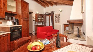 A kitchen with wooden cabinets, a red sofa, a dining table with fruits and wine glasses, and a fireplace.