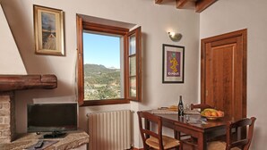 A dining area with a table, chairs, a television, and a window with a view of the countryside.