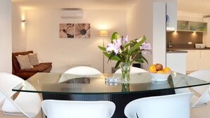 A modern dining area with a glass table, white chairs, a vase with flowers, and a bowl of fruit. - Casa La Vista - Bungalow with fantastic sea views (Mogan)