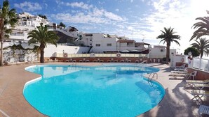 A swimming pool with lounge chairs and a supermarket in the background. - Casa La Vista - Bungalow with fantastic sea views (Mogan)