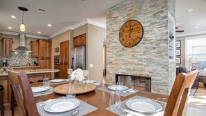 A modern kitchen with wooden cabinets, a stone accent wall, a large clock, and a dining area set for a meal.