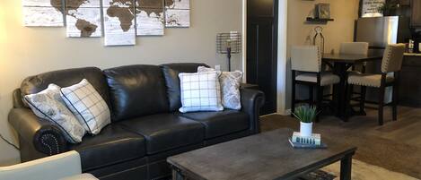 A living room with a black leather sofa, a coffee table, and a world map artwork on the wall.