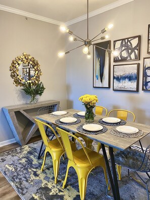 Un coin repas avec une longue table dressée pour quatre personnes, des chaises jaunes et un lustre.
