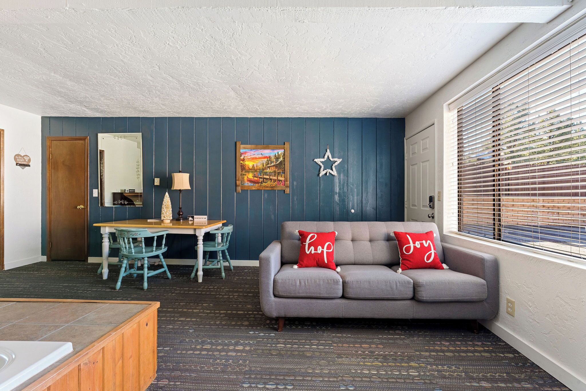 A cozy living room with a gray sofa, a wooden dining table, and blue walls.