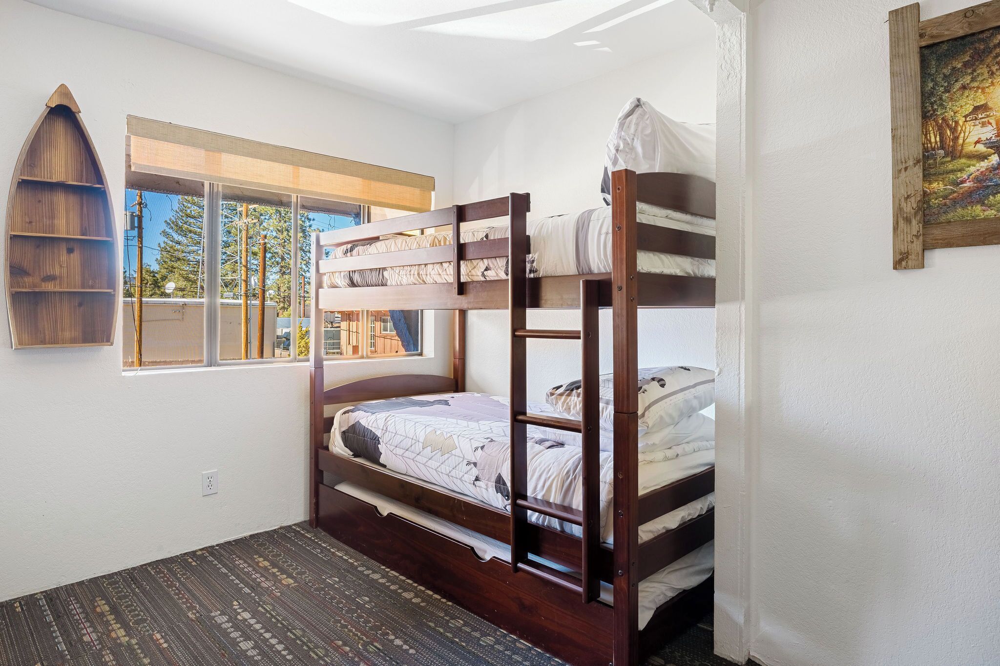 A bunk bed room with a window, a wooden shelf, and a painting on the wall.