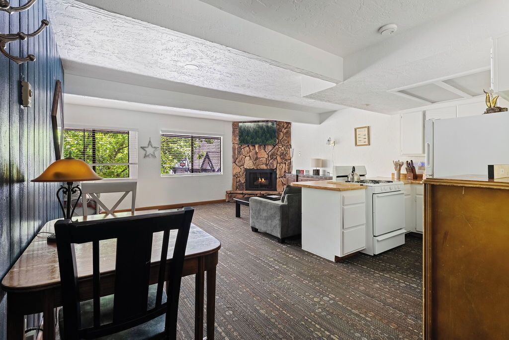 A spacious living area with a fireplace, a dining table with chairs, and a kitchen area with a stove and refrigerator.