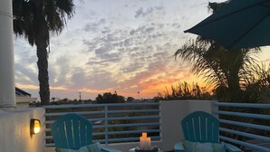 Ein Balkon mit zwei türkisfarbenen Stühlen, einem kleinen Tisch mit Kerzen und Blick auf einen Sonnenuntergang.