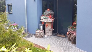 Een moderne gevel met blauwe buitenkant, een decoratieve stronk als middelpunt, en een kleine tuin met planten en een lantaarn.