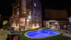 Un immeuble à plusieurs étages doté d’une piscine, d’un espace extérieur aménagé et d’une façade bien éclairée.