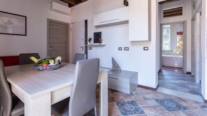 Un coin repas avec une table dressée pour deux personnes, un saladier de fruits et une cuisine moderne dotée de meubles blancs et d’un four encastré.