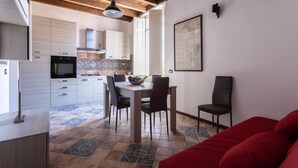 Une cuisine moderne avec des meubles blancs, une table à manger avec des chaises et un canapé rouge dans l’espace salon.