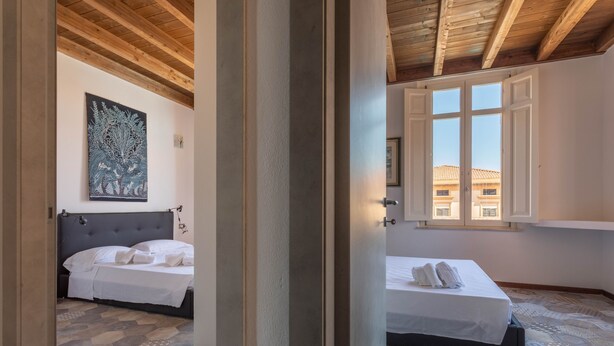 Une chambre avec deux lits, un plafond en bois, une grande fenêtre et un sol à motifs.