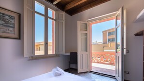 Une pièce avec un lit, une fenêtre et une porte ouverte donnant sur un balcon.