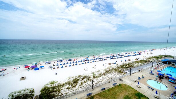 A beach with white sand, a pool, and umbrellas.