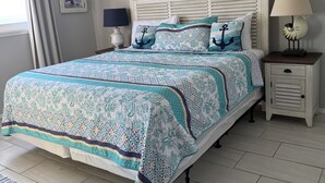 A neatly arranged bedroom with a large bed, a bedside table, a lamp, and a framed picture on the wall.
