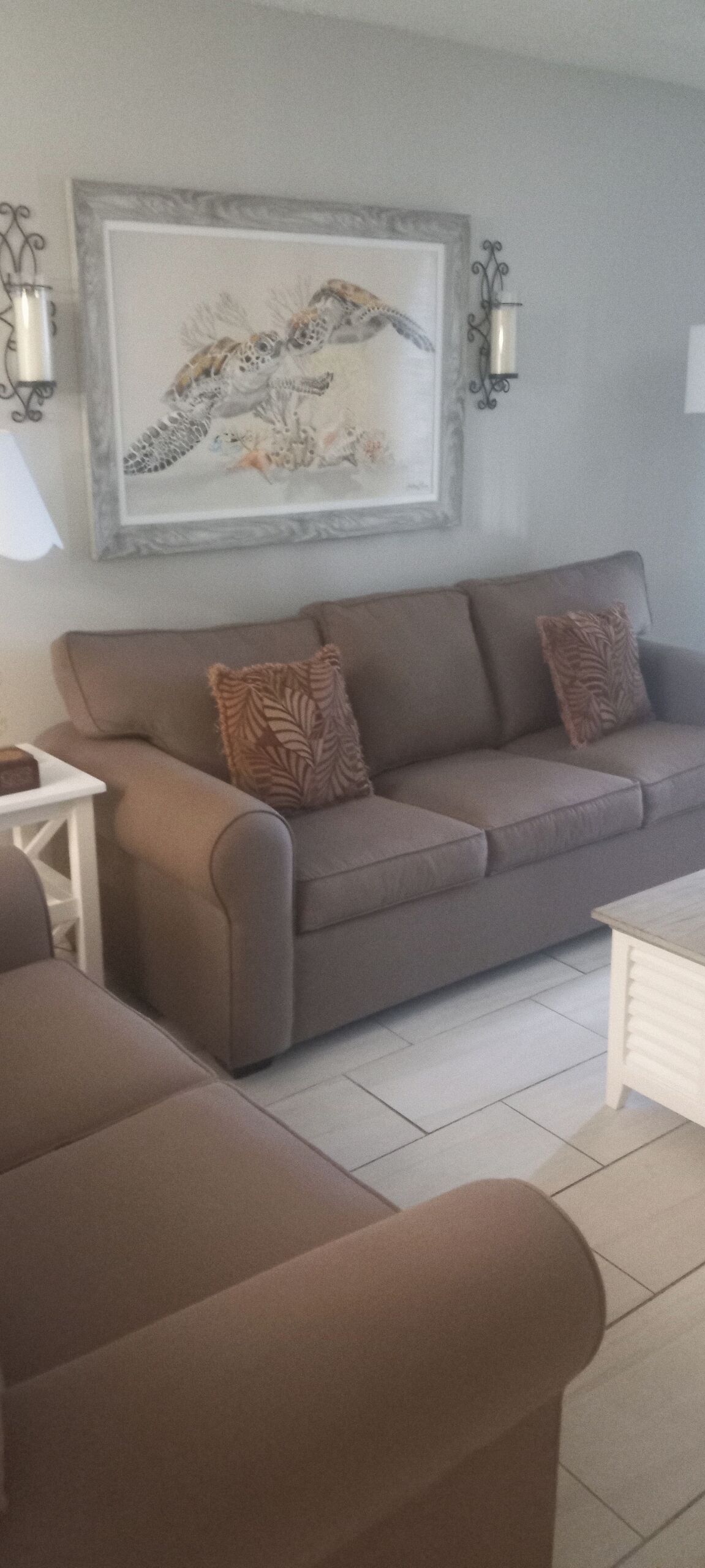 Una sala de estar con un sofá marrón, dos sillones a juego, una mesita de noche blanca y una obra de arte enmarcada en la pared.